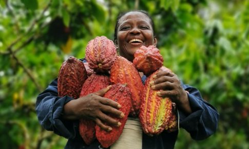 A woman laughing and holding onto a large amount of cacao fruit.